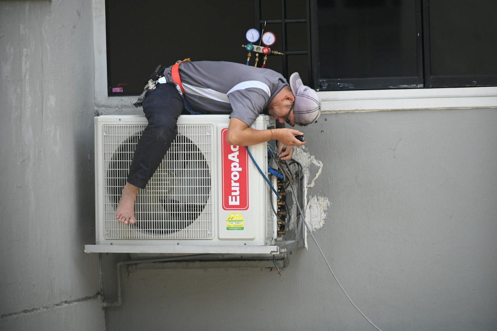 Adelaide installer fitting a Daikin split-system air conditioner above a brick veneer living-room wall, vacuum gauge connected, late-afternoon light